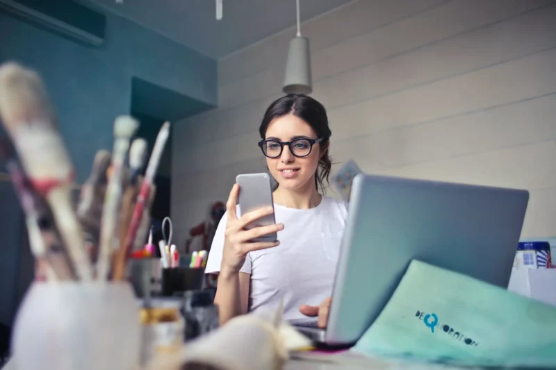 Woman in glasses using smartphone and laptop reading summer updates